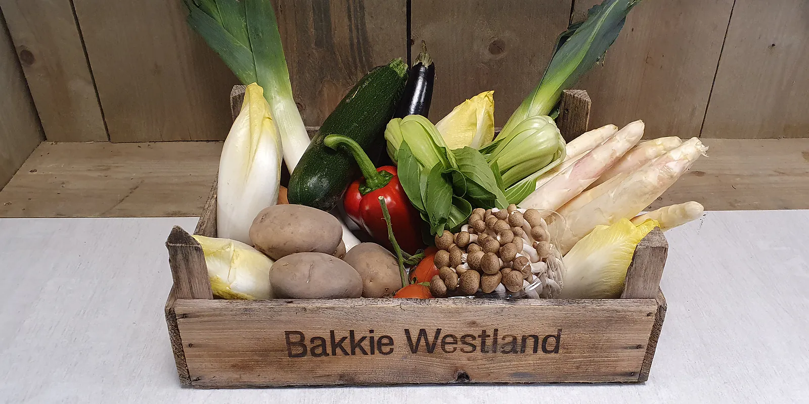 Groentebox medium in een Bakkie Westland-kistje op Joe's plank: prei, courgette, aubergine, witlof, paprika, paksoi, asperges, aardappels en champignons.