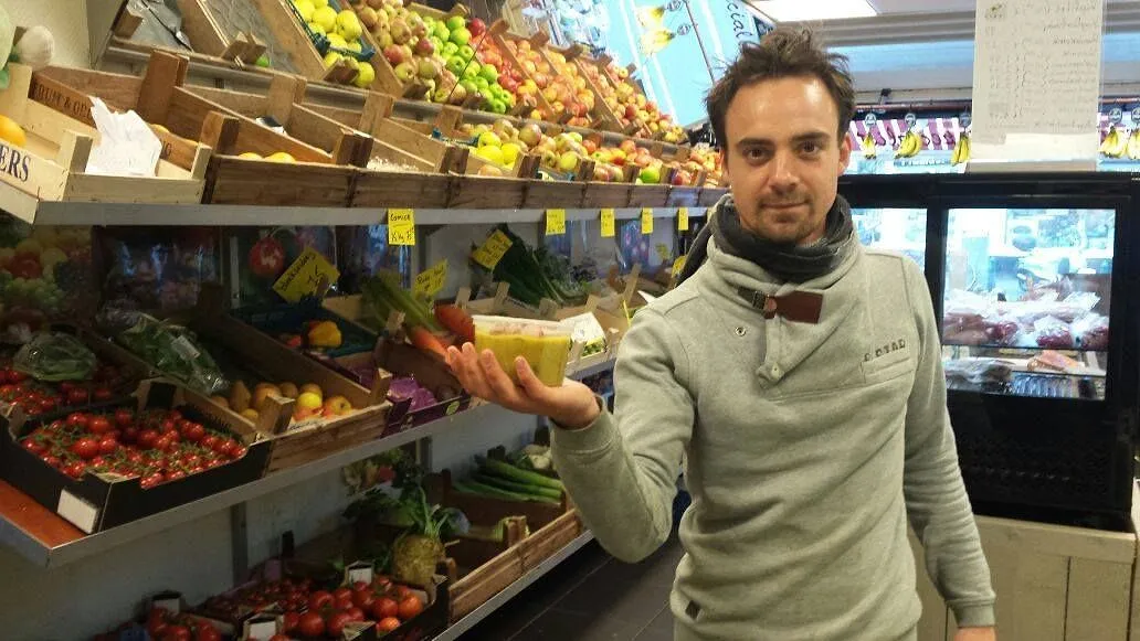 Joe tussen de schappen met fruit en groente, met een bakje in zijn hand.