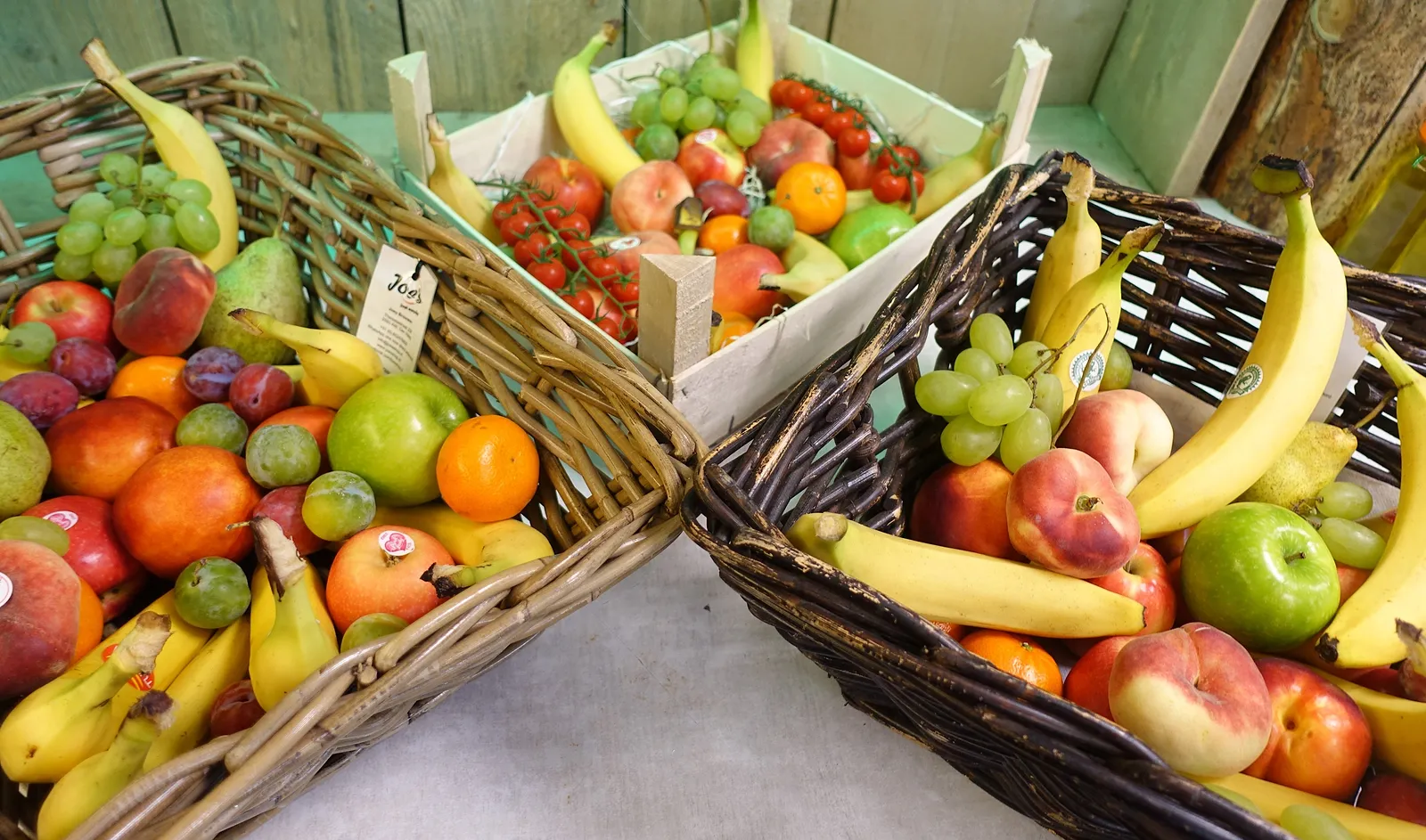 Rieten manden vol fruit voor op kantoor: bananen, appels, peren, sinaasappels, druiven en perziken.