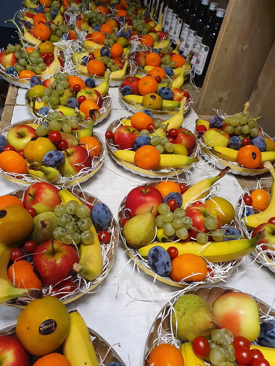 Een tafel vol fruitschalen met appels, sinaasappels, bananen, druiven en pruimen, klaar om te bezorgen.